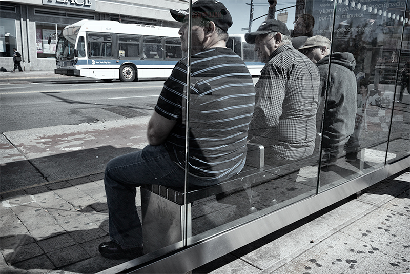 Three men at bus stop, all looking to left for bus to arrive.