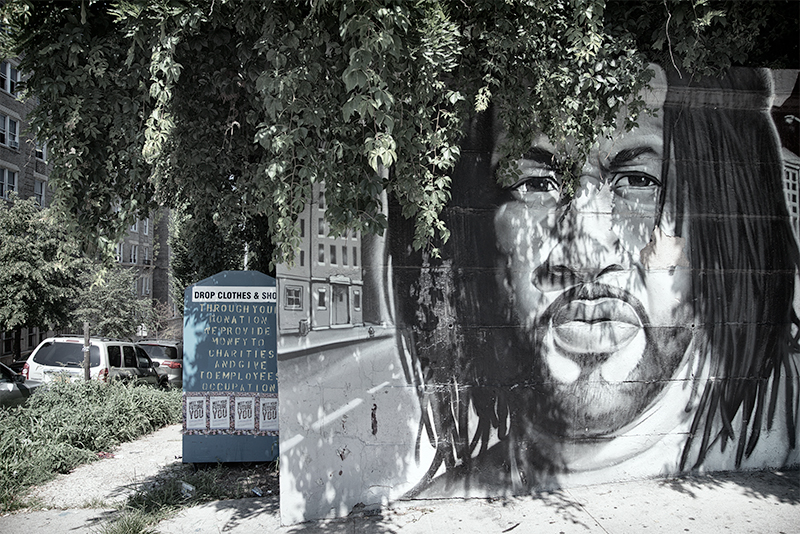 The mural of DJ Kool Herc next to a bin for clothing donations.