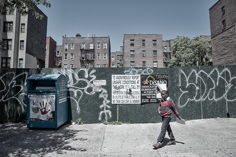 Young man passing green wall blocking construction area. Sign provides info to anonymously report violations.