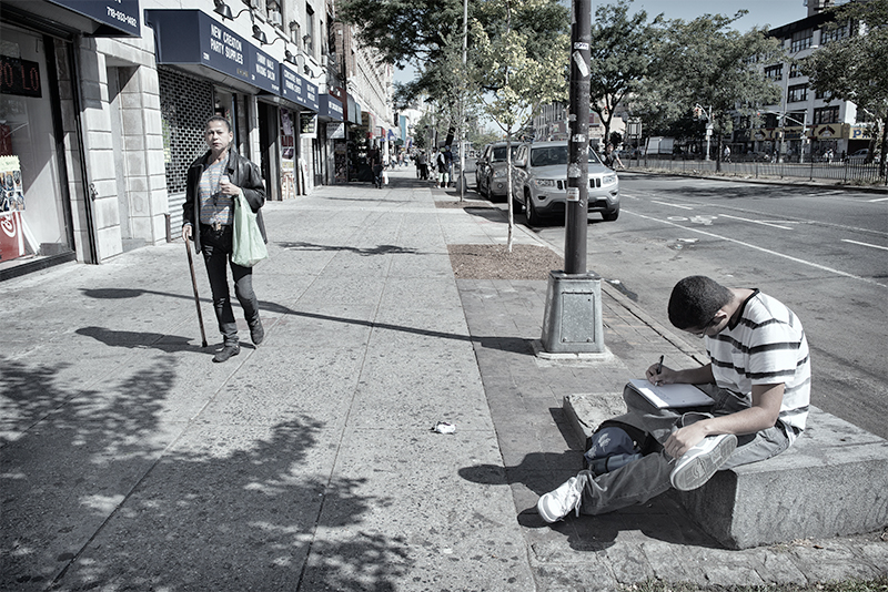 Young man doing homework; woman with cane approaching.