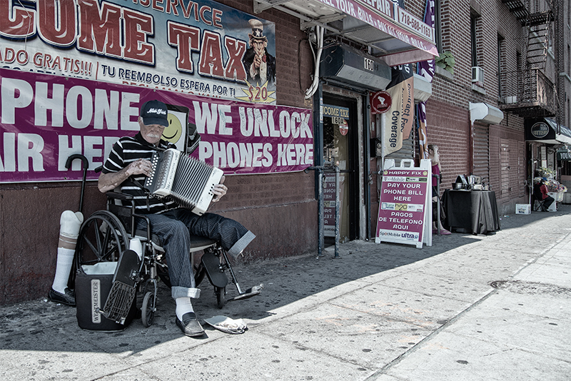 Man with prosthetic leg plays accordion in front of store that advertises "we unlock phones." 