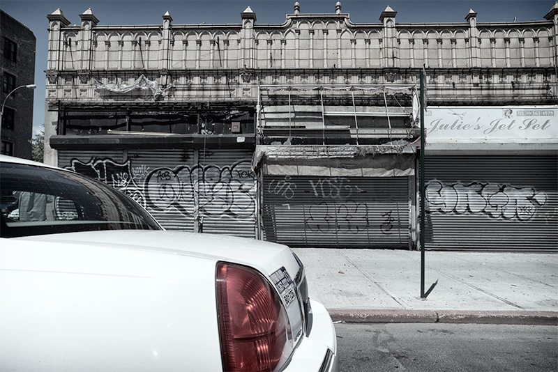 White limo passes old building with storefront gates and the sign "Julie's Jet Set."