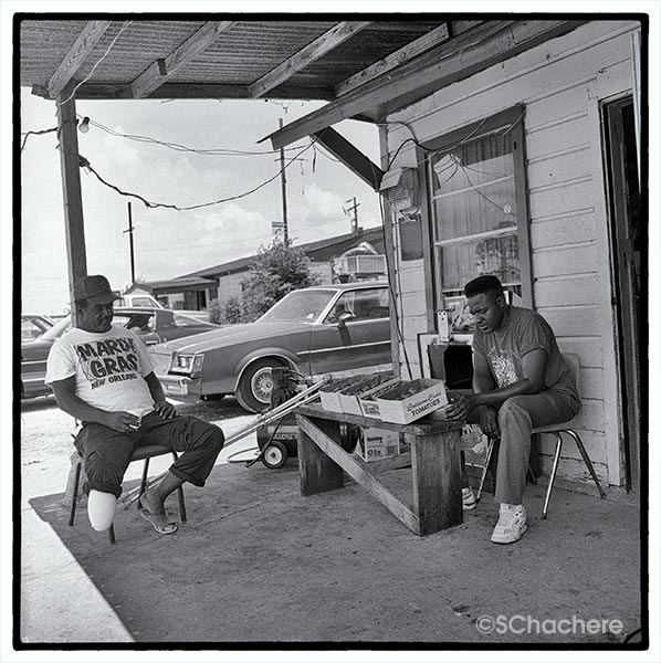 Men sitting under overhang, selling tomatoes